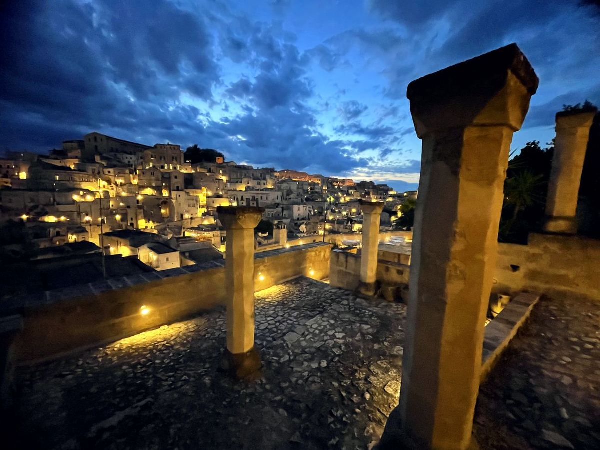 Die Steinsäulen der Terrasse zur blauen Stunde, dahinter die beleuchteten Sassi von Matera